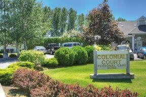 A landscaped area with a sign reading 'Colonial Court', surrounded by trees and parked cars.