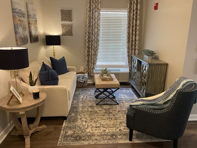 A cozy living room with a white sofa and armchair, accented by decorative pillows and a patterned rug.