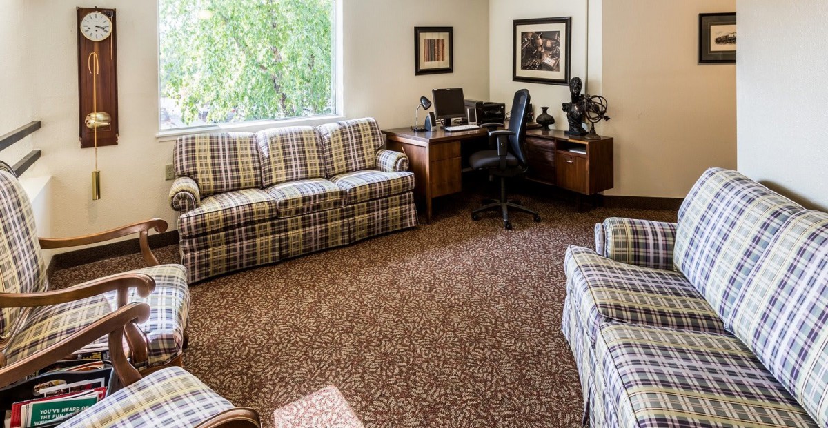 A cozy living room with an integrated office space, featuring plaid sofas and a neatly organized desk area.