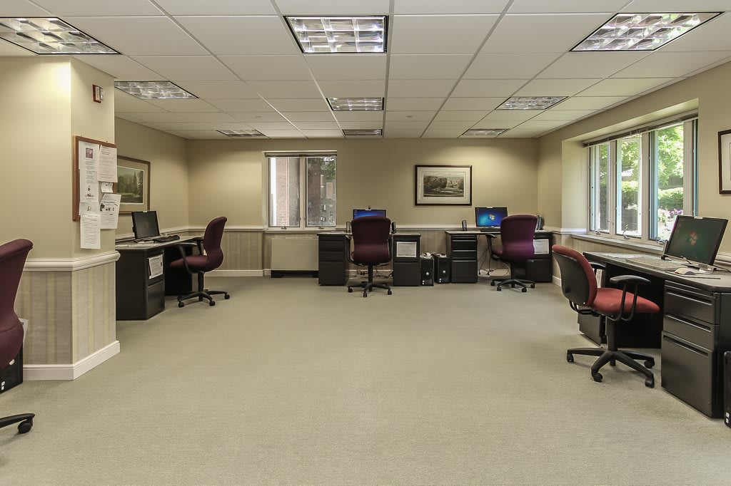 A spacious office with multiple desks and computers, featuring large windows and comfortable seating.
