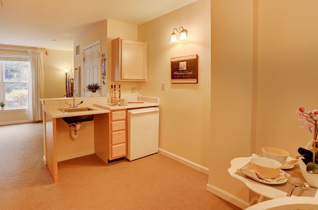 Compact kitchenette area with wooden cabinets, a small fridge, and warm lighting.