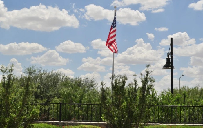An American flag waving under a bright, cloudy sky with trees in the background.