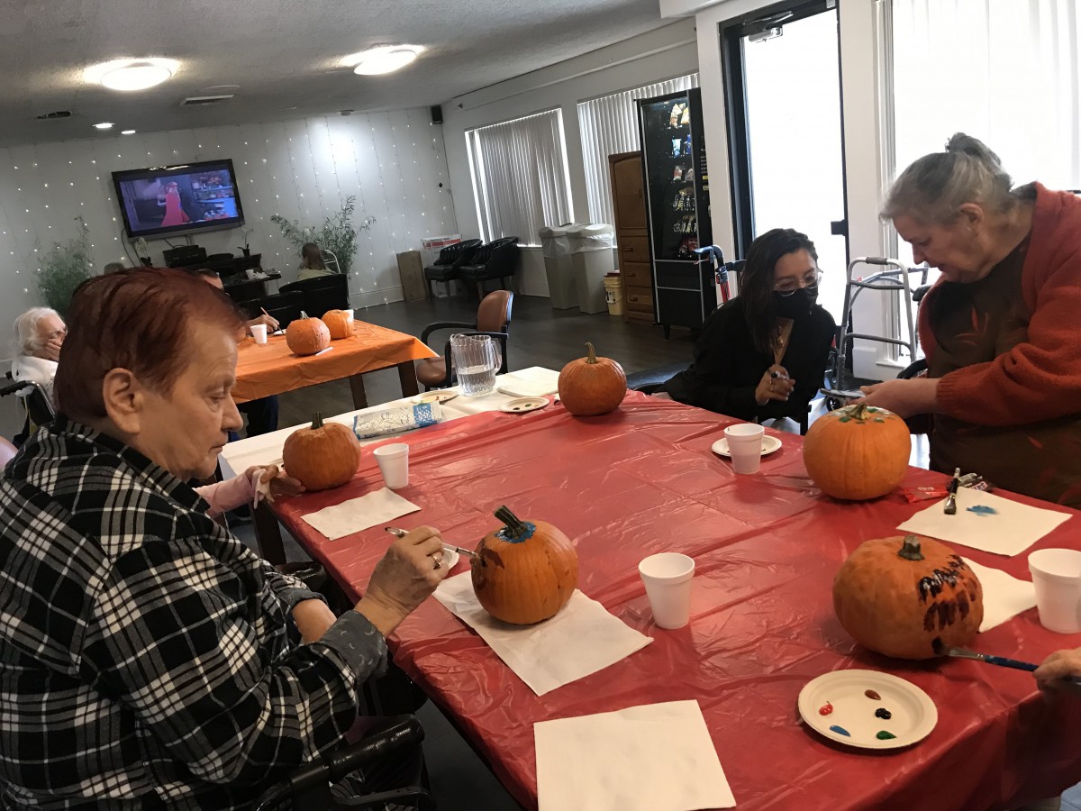 A group of people participating in a pumpkin painting activity indoors.