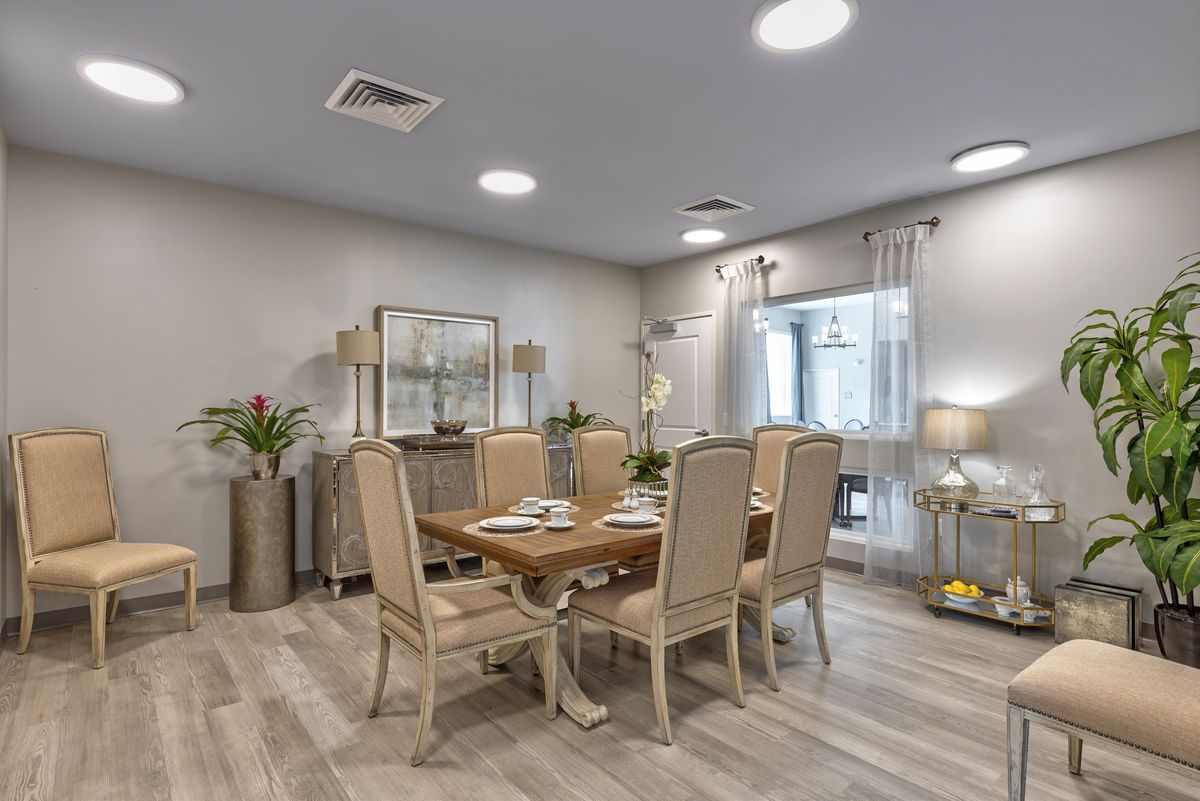 A modern dining room with a wooden table and elegant chairs, decorated in neutral tones with stylish lighting and greenery.