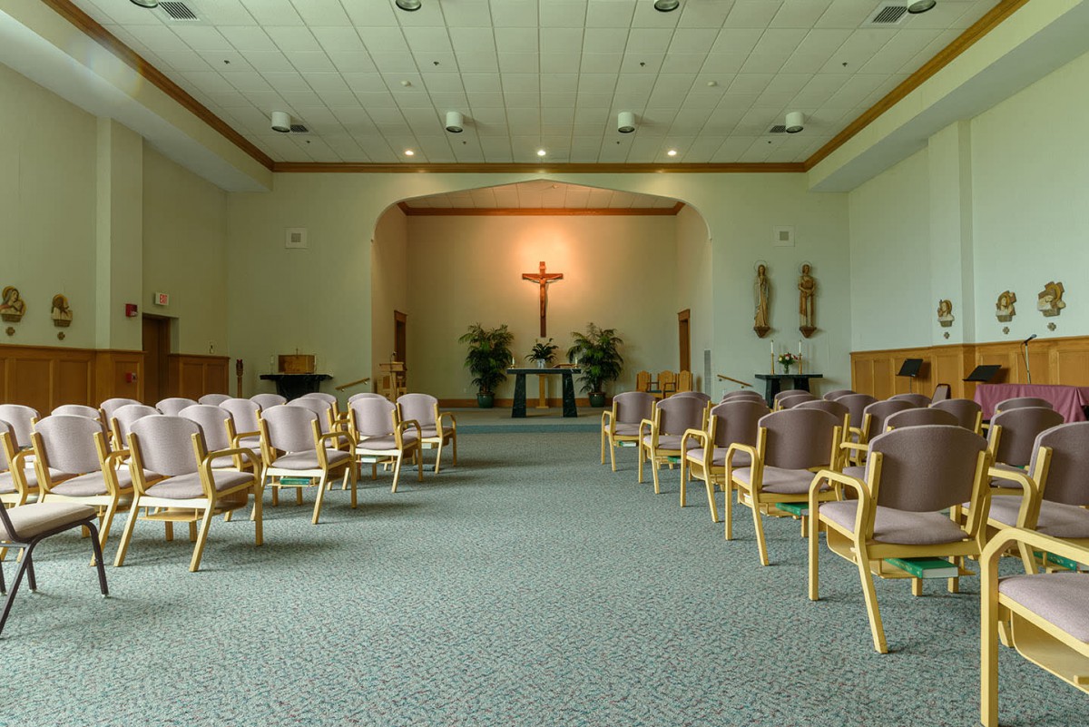 An interior view of a chapel with rows of chairs and a cross at the front.