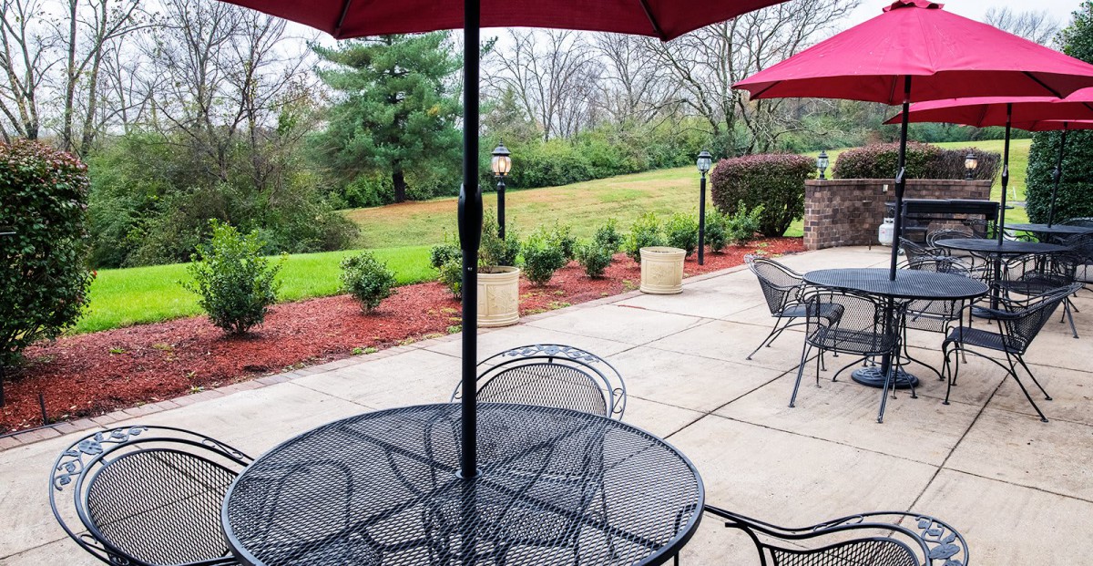 A peaceful outdoor patio setup with tables, chairs, and umbrellas overlooking a garden landscape.