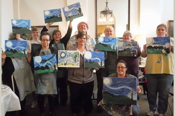 A group of adults proudly displaying their landscape paintings during an art class.