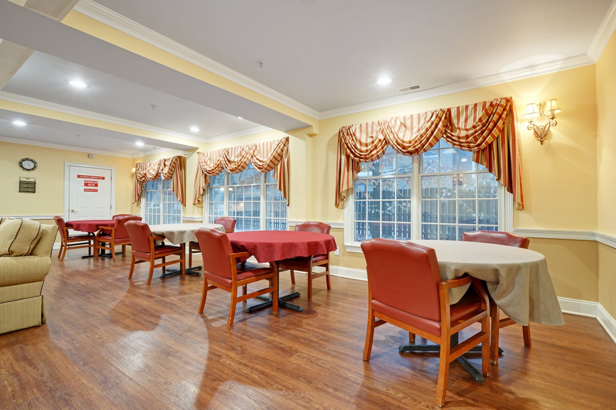 A well-lit dining room with neatly arranged tables and chairs, adorned with decorative curtains and large windows.