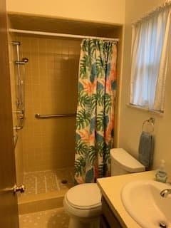 A small bathroom with a tropical-themed shower curtain, toilet, and sink.