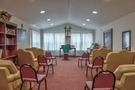 A small chapel interior with chairs arranged facing an altar and cross.