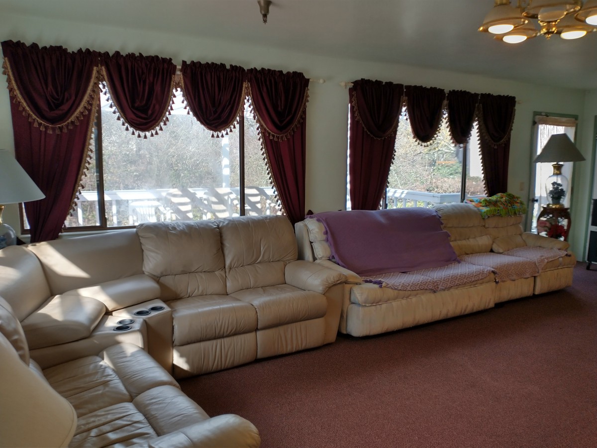 A cozy living room with a beige sectional sofa and large windows adorned with dark red curtains.