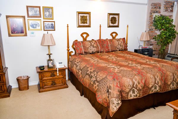 A cozy bedroom with a patterned bedspread, matching lamps, nightstands, and framed artwork on the wall.