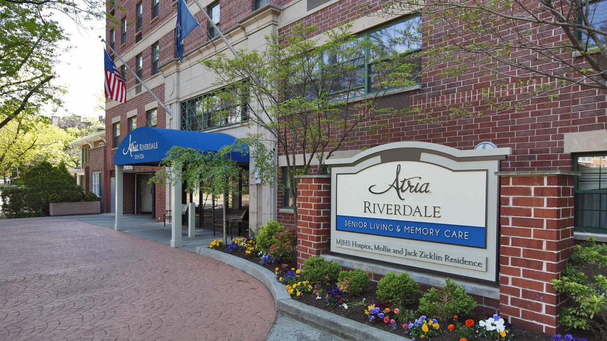 Entrance to a building with a blue awning and adjacent signage for a senior living community.