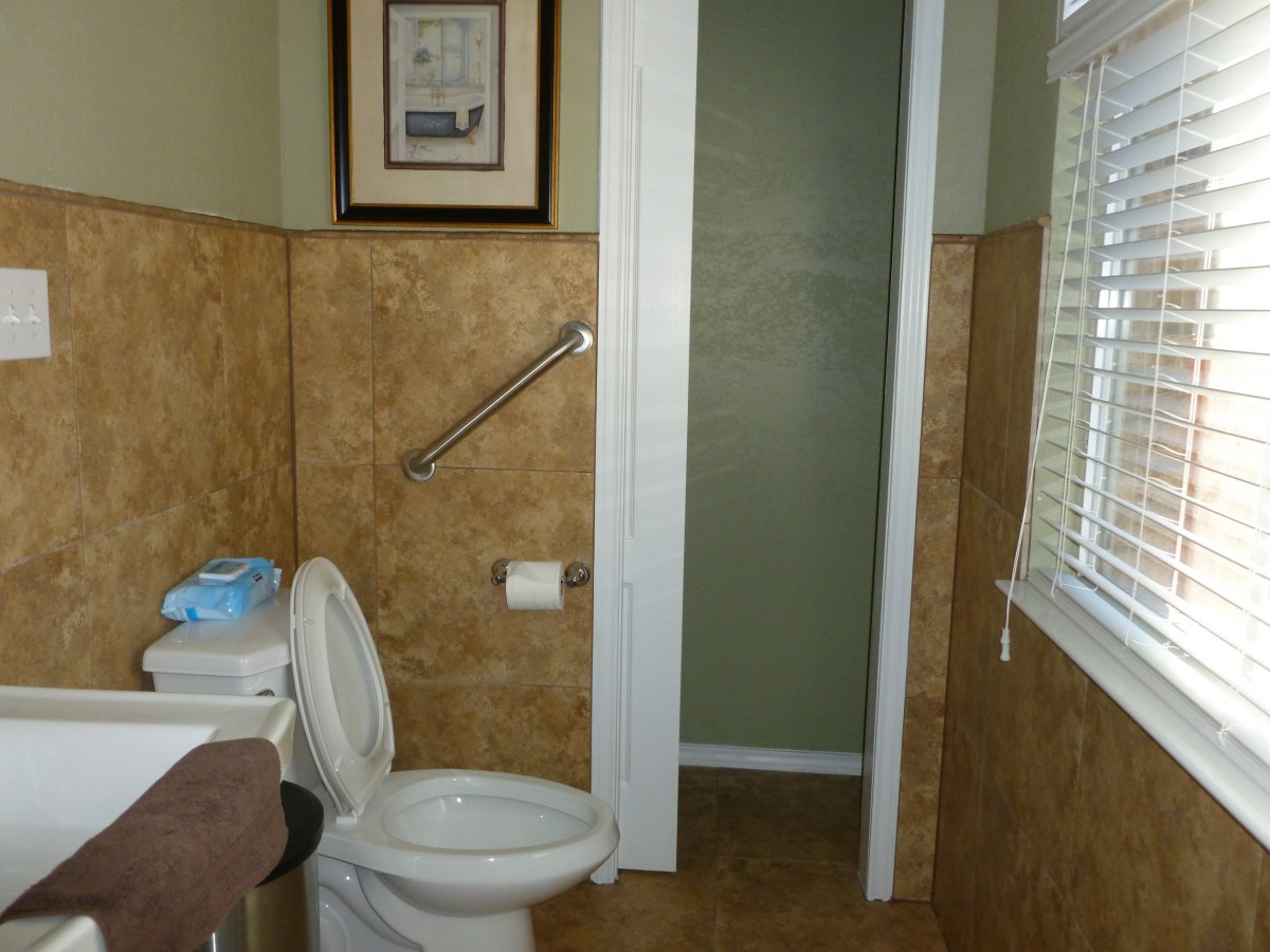 A bathroom with a toilet, tiled walls, and a grab bar near the window.