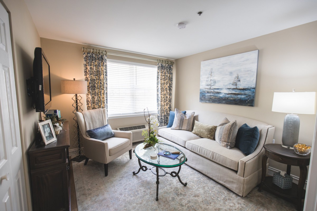 A cozy and elegantly decorated living room with a sofa, armchair, coffee table, and large window.