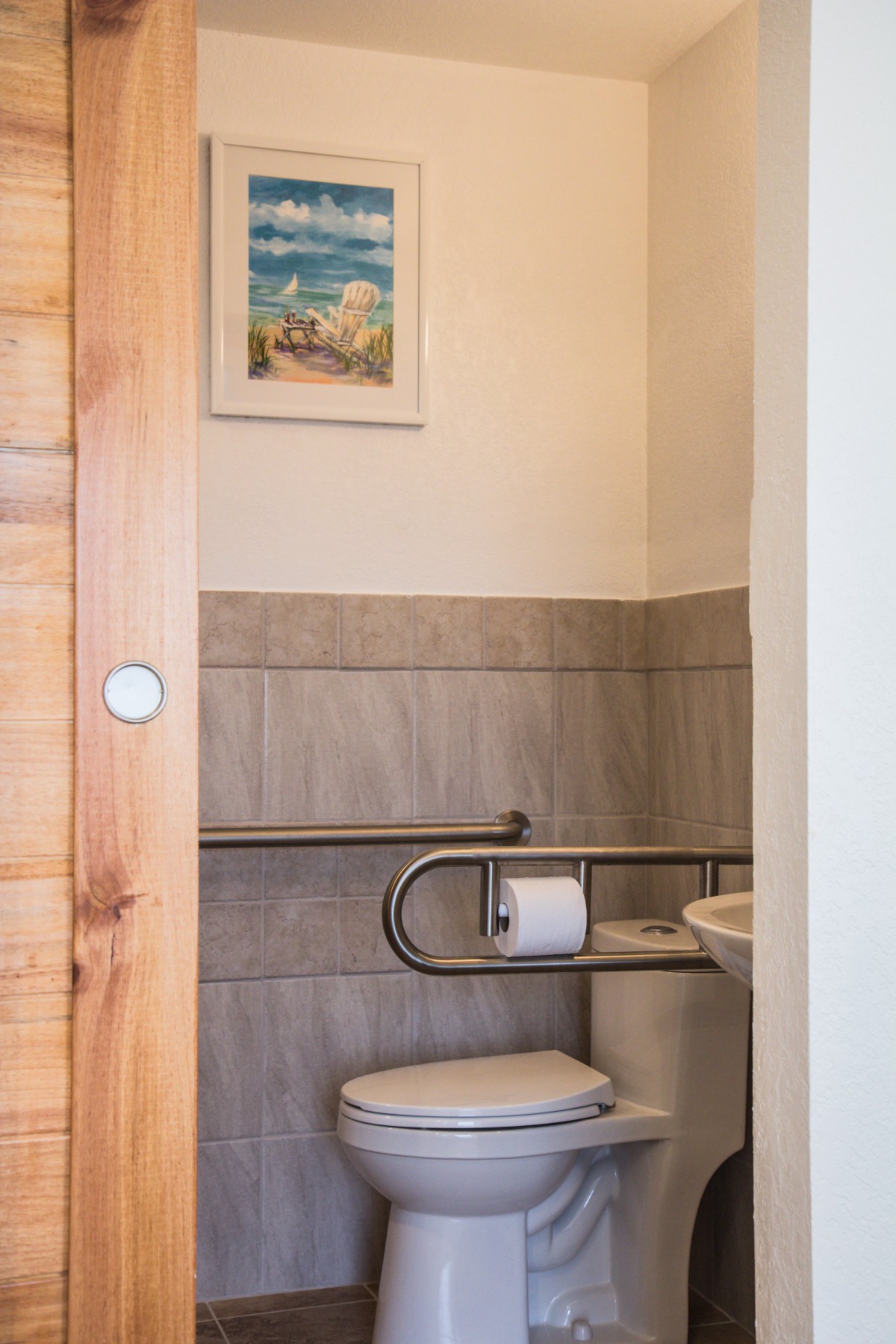 A small bathroom with a toilet, sink, and handrail.
