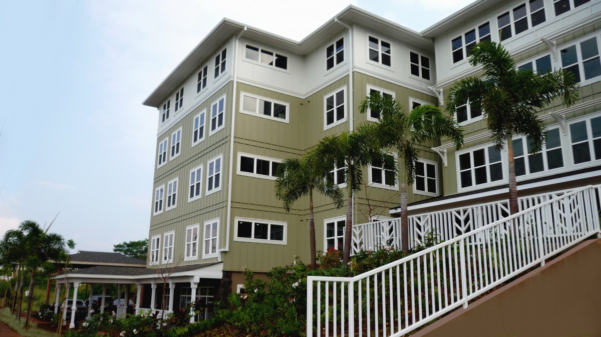 A four-story residential building with a green facade and white-trimmed windows, surrounded by palm trees.