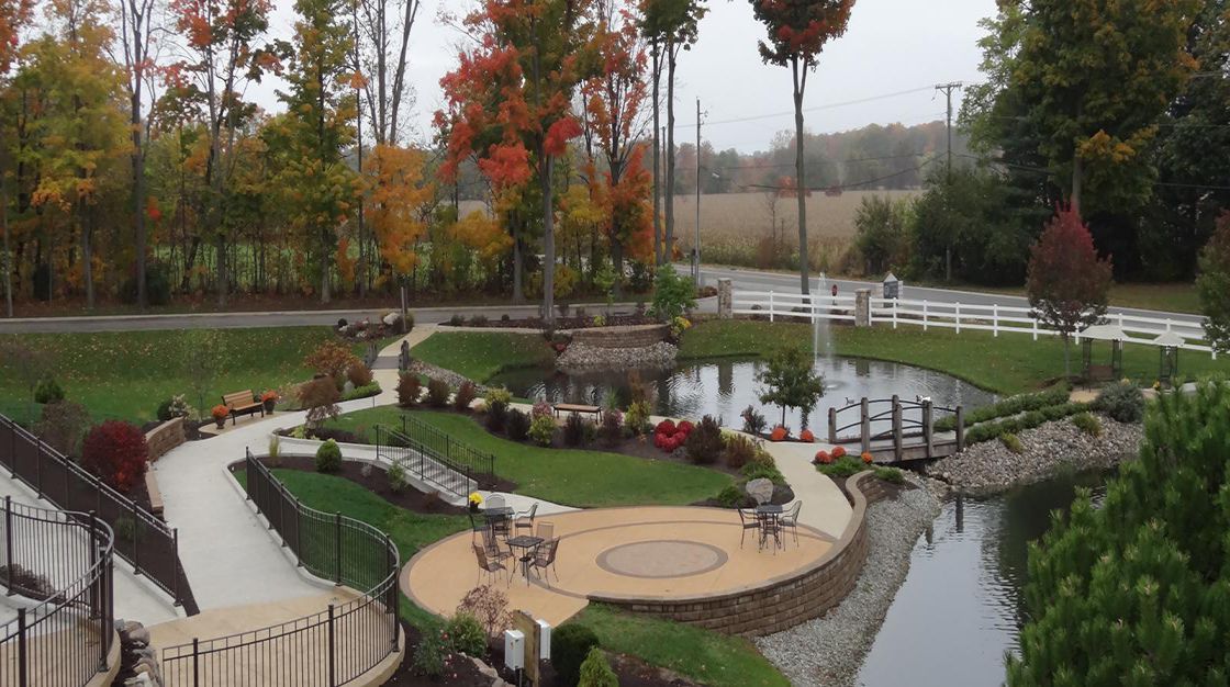 A beautifully landscaped garden featuring a pond, walkways, and autumn-colored trees.