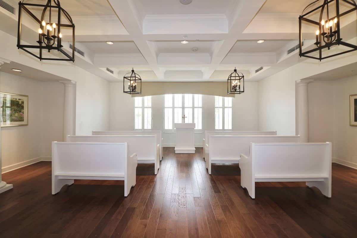 A serene chapel interior featuring white pews and wooden flooring.