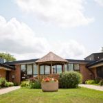 A single-story brick building with a garden and a cloudy sky.