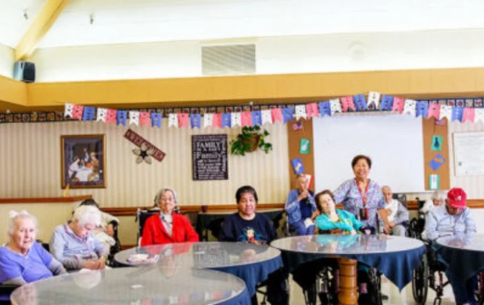 A group of elderly individuals gathered indoors, possibly celebrating an event with festive banners.