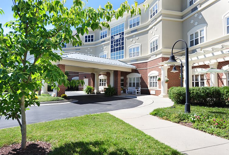 A modern building entrance with well-maintained landscaping and a sidewalk under a clear blue sky.