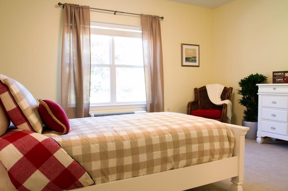 A cozy bedroom with a checkered bedspread, large window, and comfortable chair.