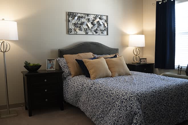 A cozy bedroom featuring a bed with patterned bedding, flanked by nightstands and a lamp, with artwork above the headboard.