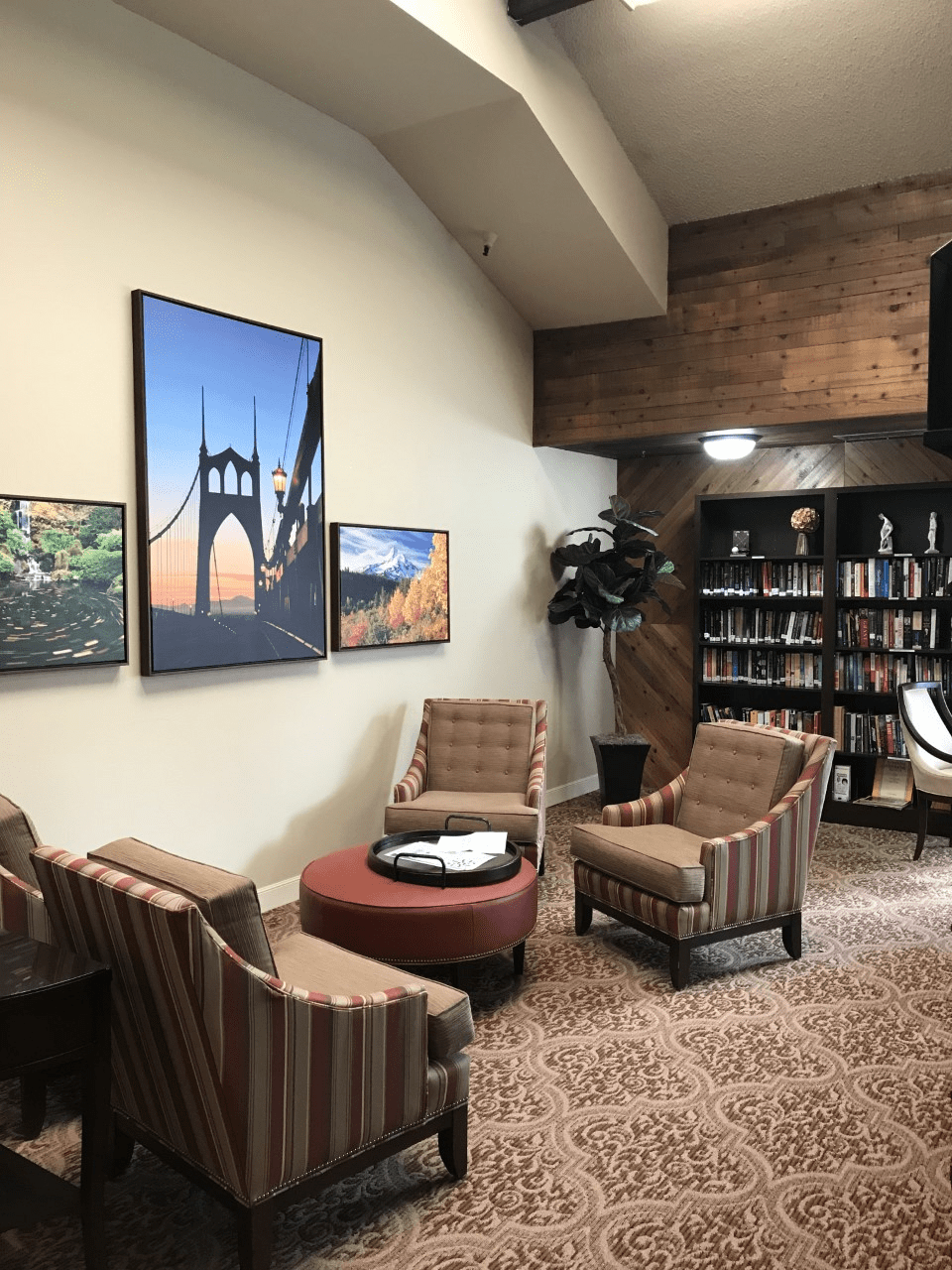 A cozy library corner with comfortable seating, artwork on the walls, and a bookshelf filled with books.