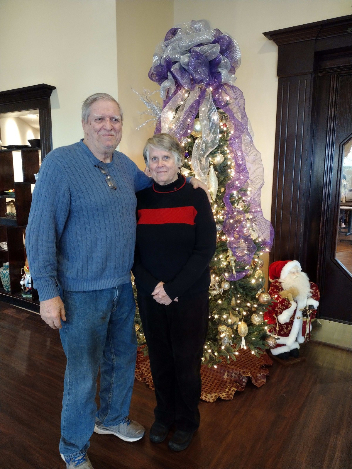 A couple standing in front of a decorated Christmas tree indoors.