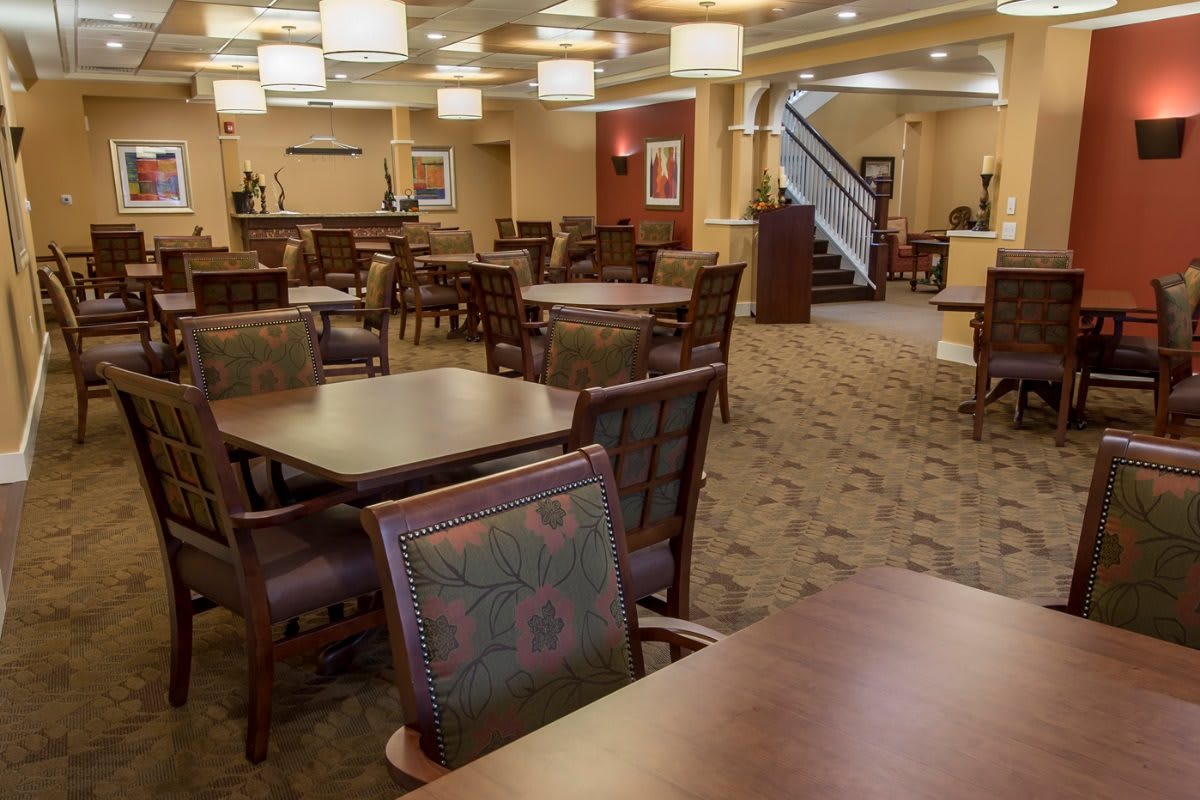 A well-lit dining area with multiple tables and chairs, featuring a carpeted floor and formal ambiance.