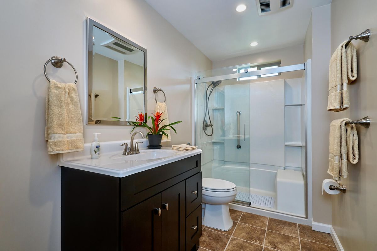 A modern bathroom with a walk-in shower, vanity with sink, and large mirror.