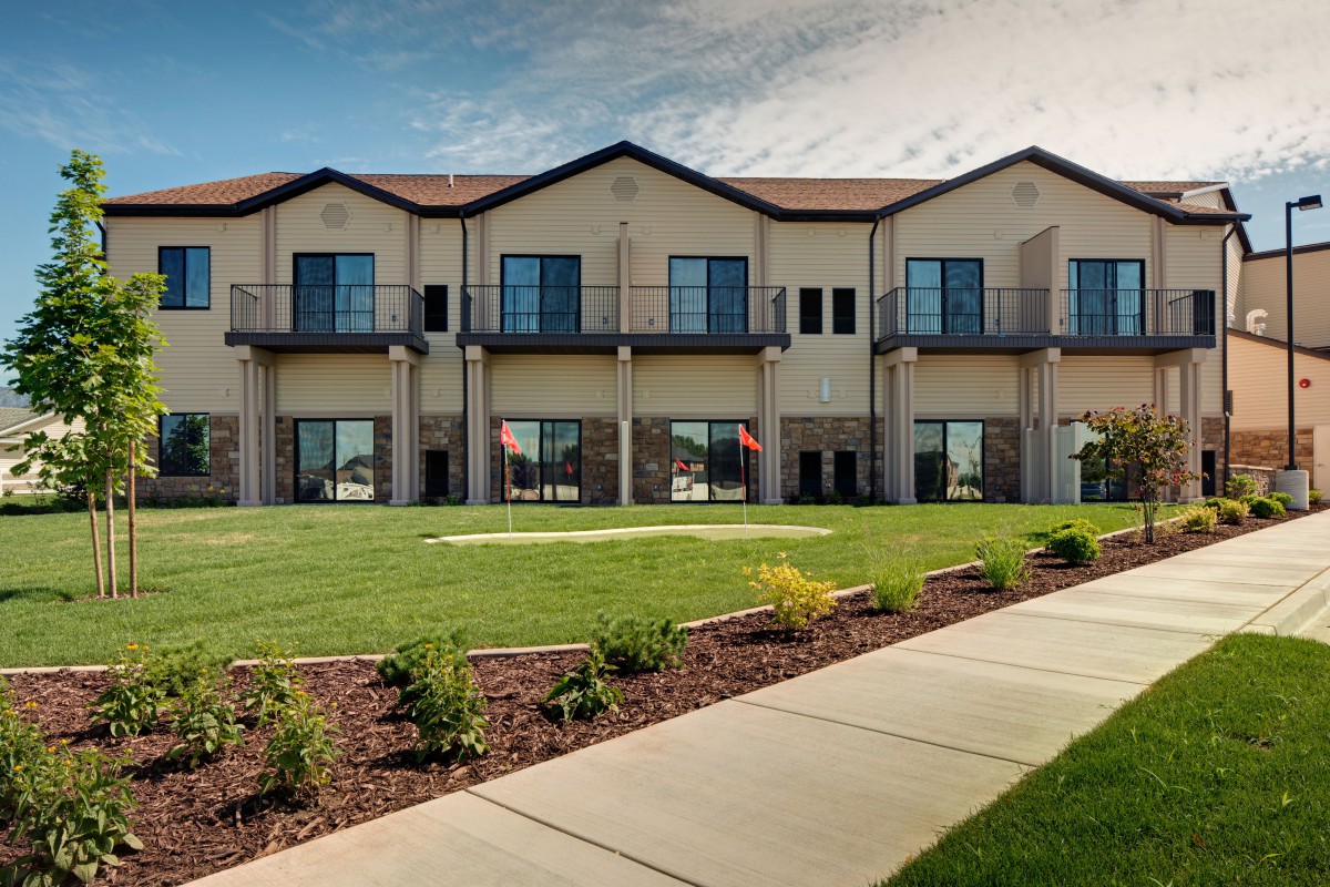 A modern two-story building with large windows, surrounded by a neatly landscaped lawn and paved pathway.