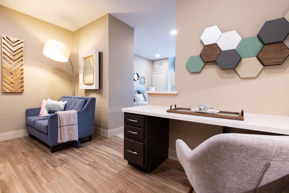 A modern living area featuring a cozy chair, wooden floors, and a stylish desk with geometric wall decor.