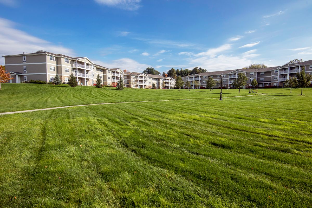 A spacious apartment complex with a large grassy area in the foreground under a clear blue sky.