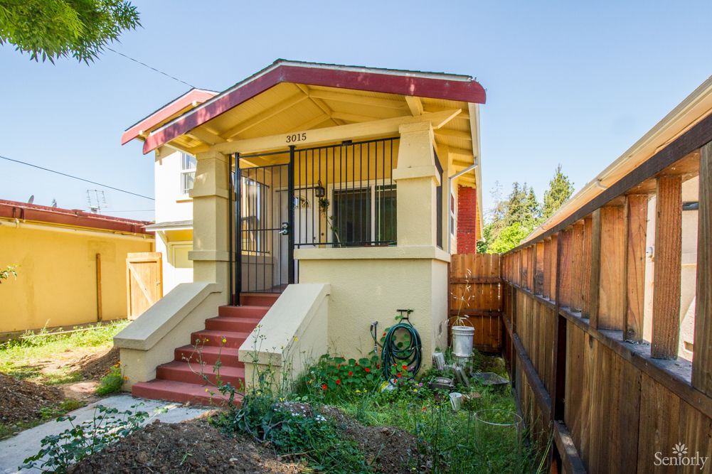A small residential house with a front porch and a fenced yard.