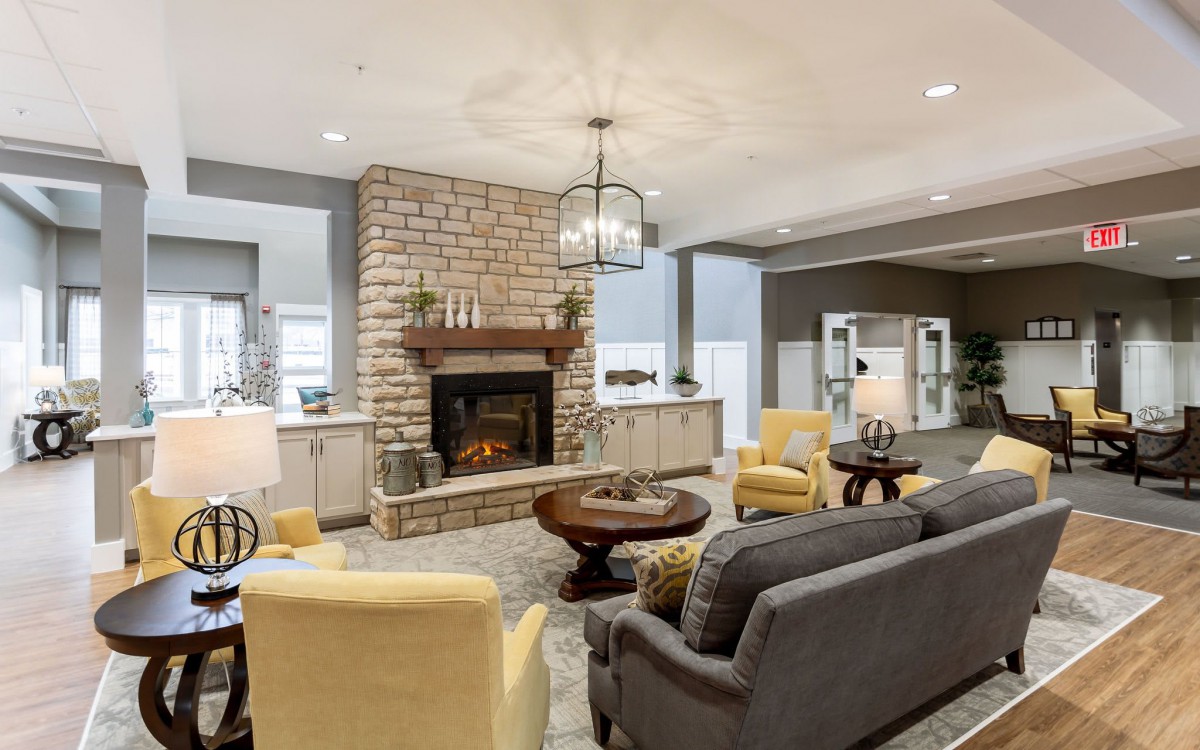 A cozy living room featuring a stone fireplace, gray sofa, yellow chairs, and elegant modern decor.