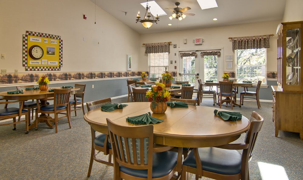 A well-lit dining room with neatly arranged tables and chairs, featuring floral centerpieces for decoration.