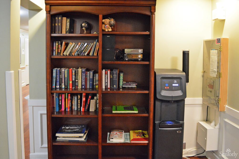 A wooden bookshelf filled with books next to a water cooler in an office setting.