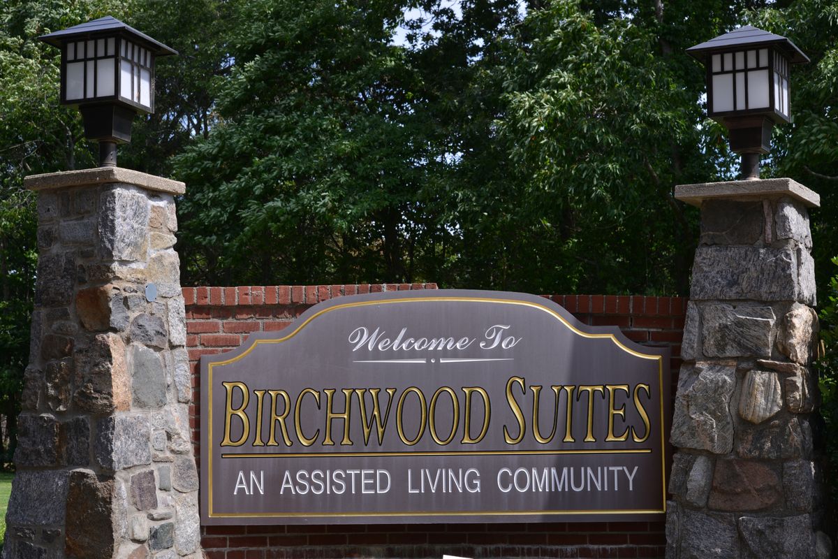 An outdoor sign for Birchwood Suites, an assisted living community, surrounded by stone pillars and greenery.