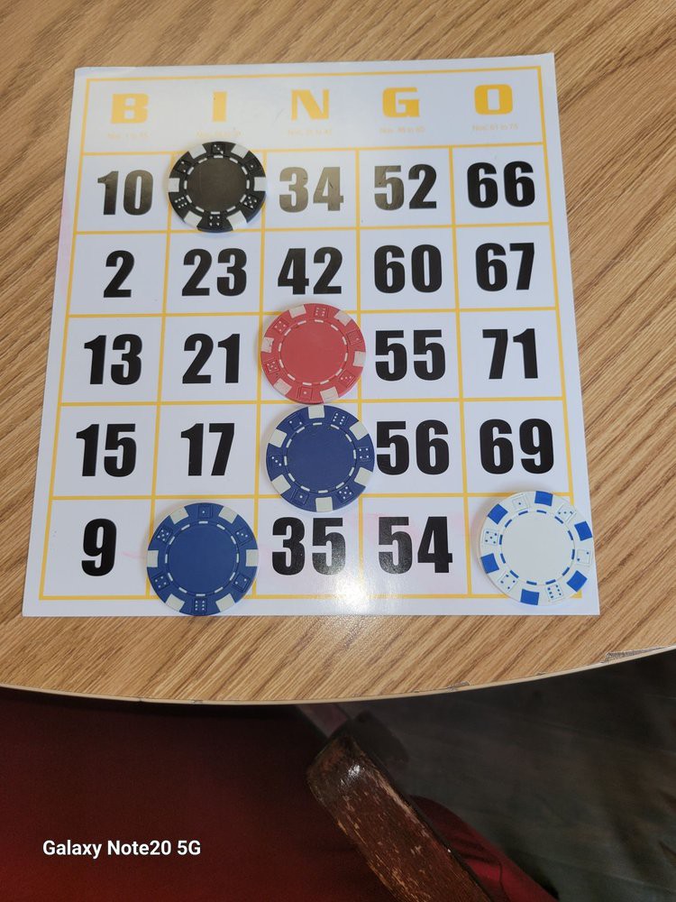 A bingo card on a table with some numbers covered by chips.