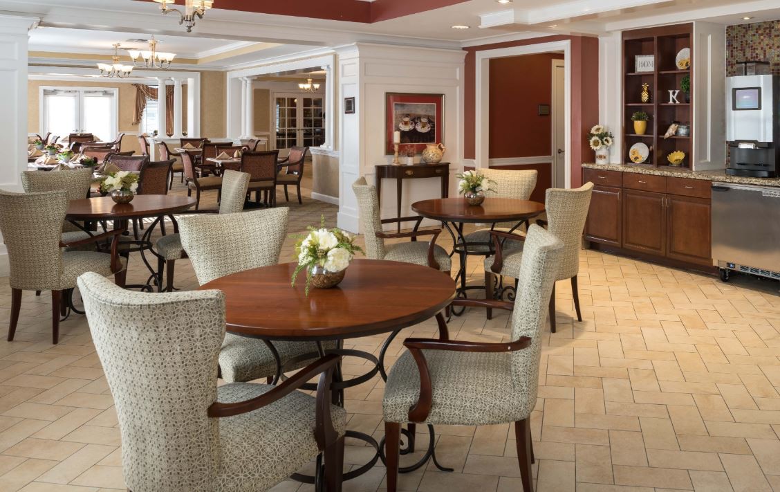 A cozy dining area with round tables and upholstered chairs, decorated with small flower arrangements.
