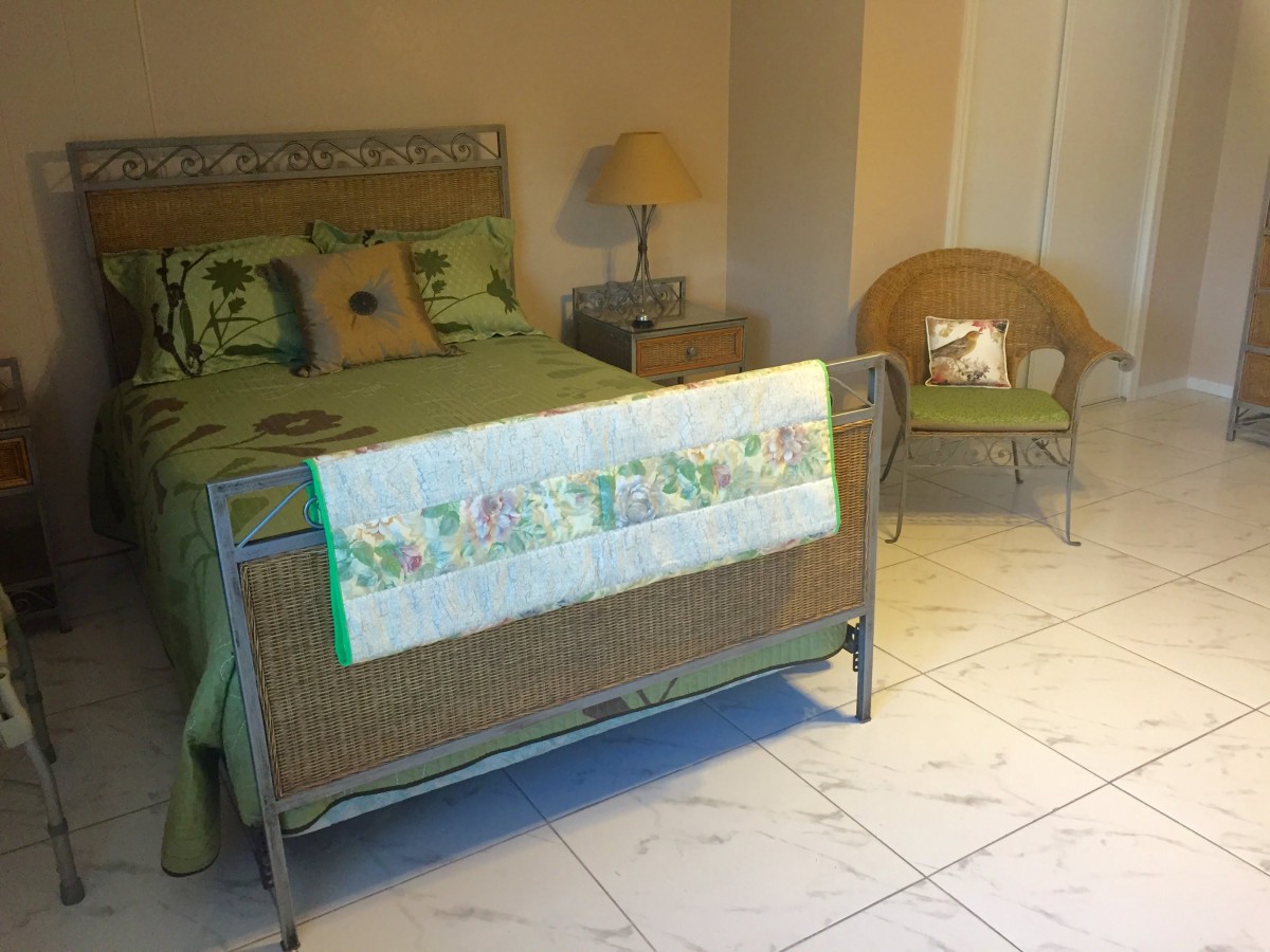 A cozy bedroom featuring a metal bed with green accents, a wicker chair, and a bedside lamp.