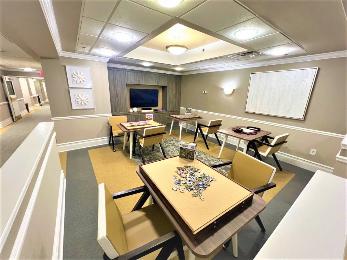 A well-lit room featuring several tables and chairs, with a puzzle in progress on one table.