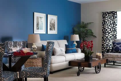 A stylish living room with a blue accent wall, featuring a comfortable sofa, decorative cushions, elegant lamps, and vibrant plants.
