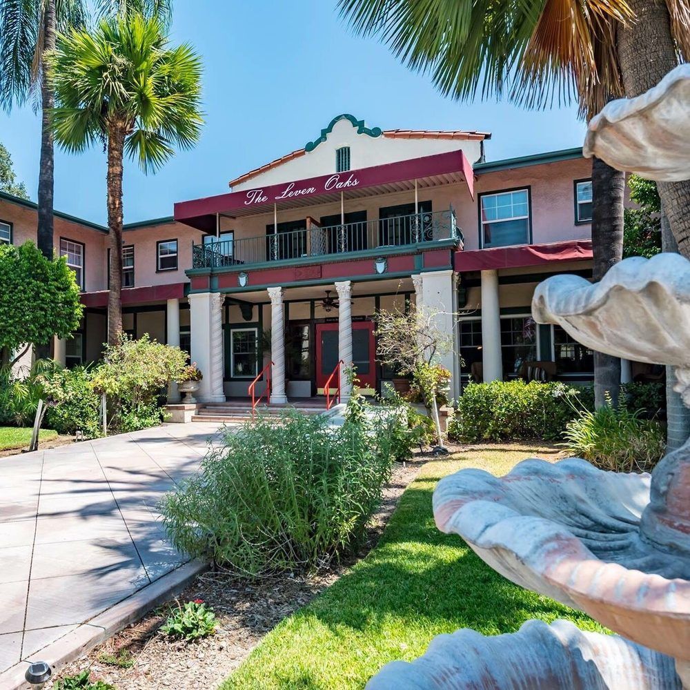 A picturesque view of a building with a fountain, surrounded by palm trees and landscaped gardens.