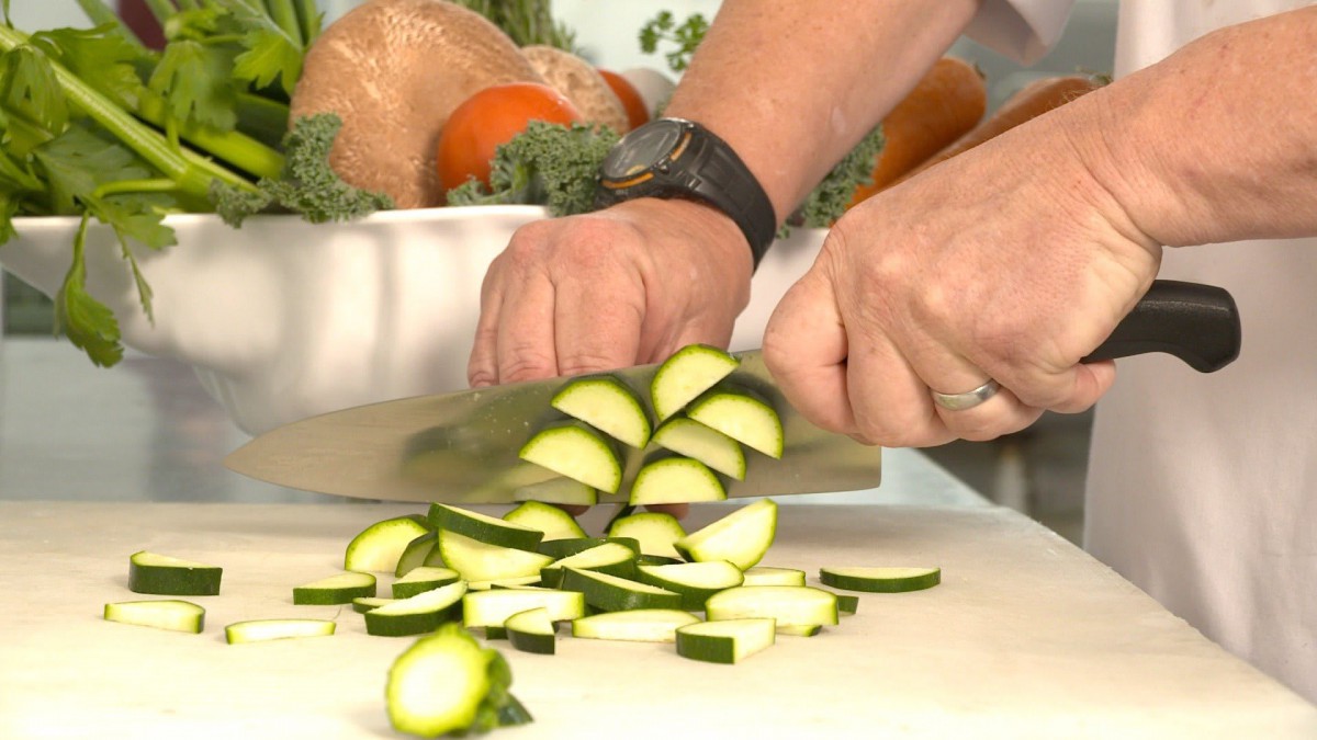 A person chopping zucchini in a kitchen setting.