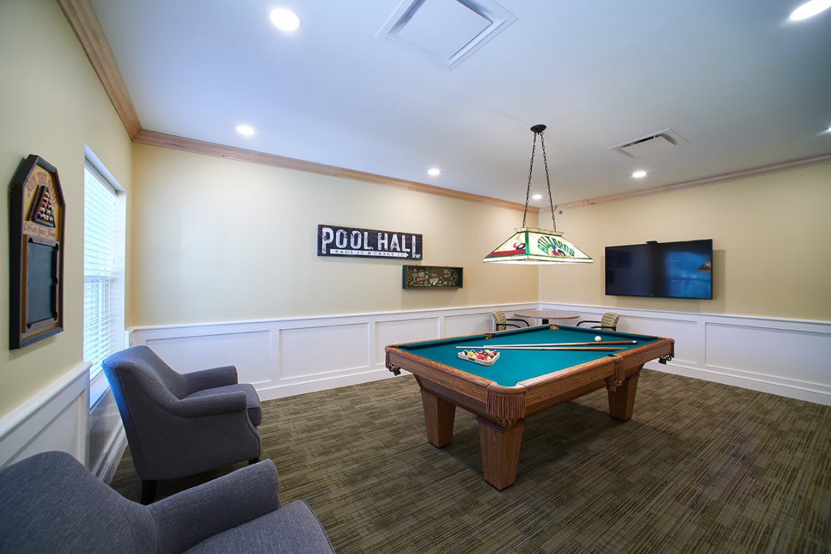 A modern game room featuring a pool table under stylish lighting, with comfortable seating and a wall-mounted TV for entertainment.