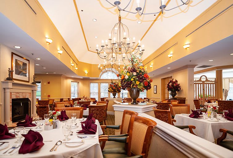 An elegant dining room with chandeliers, featuring neatly set tables and floral arrangements.