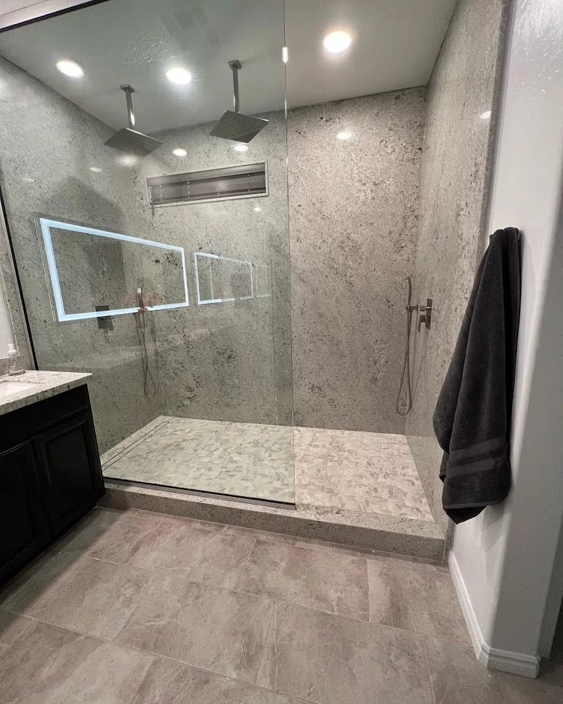 A modern bathroom featuring a spacious glass-enclosed shower with elegant tile walls and a lighted mirror.